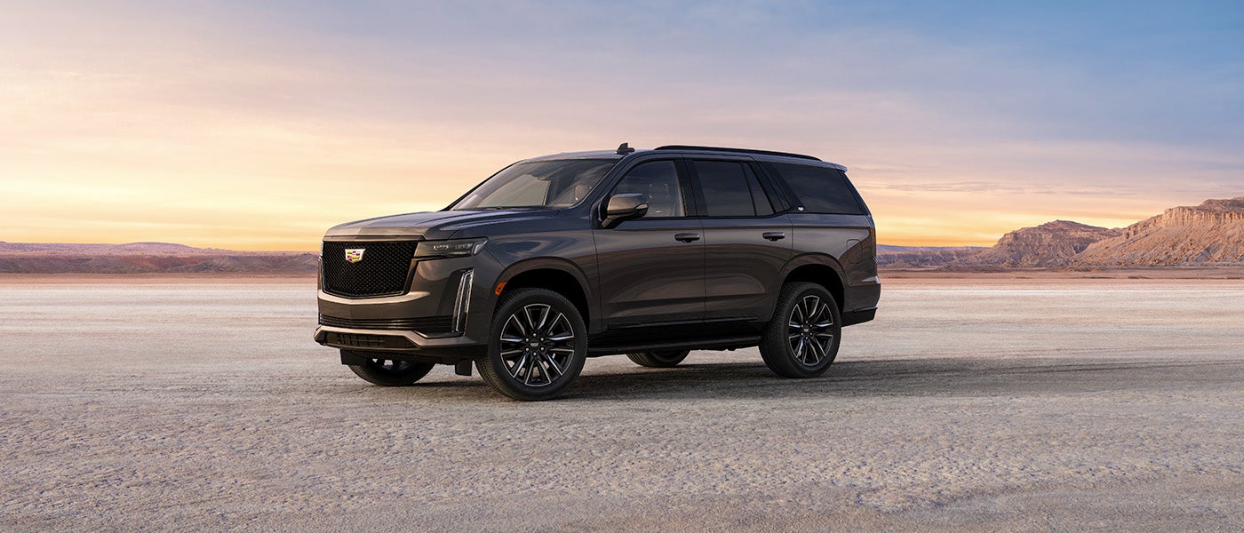A 2024 Cadillac Escalade parked in a vast desert landscape under a clear blue sky.
